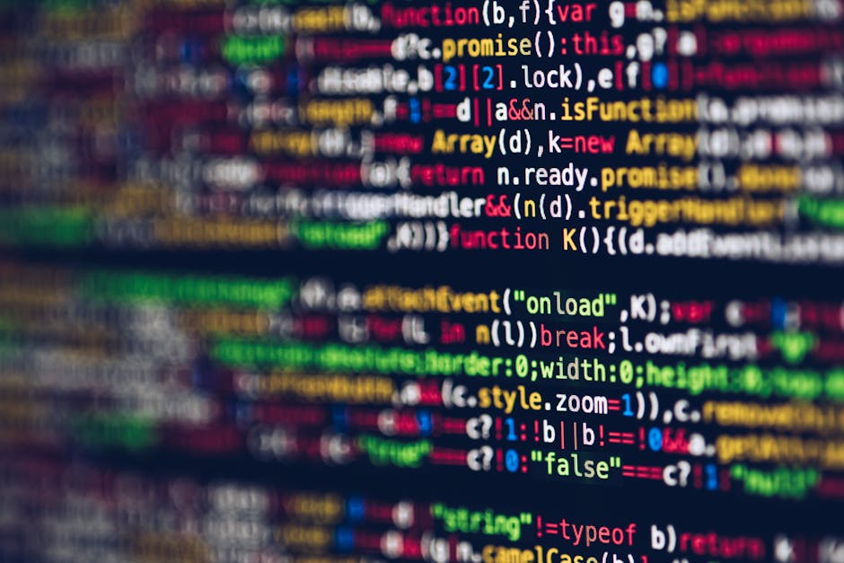 A close-up view of a computer screen displaying lines of colorful code on a dark background, with red, green, blue, and purple text representing different coding elements. The display appears slightly